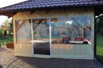 Przezroczysta osłona tarasowa na wymiar z oknem, osłaniająca altanę z jacuzzi i meblami ogrodowymi.