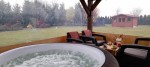 Przeźroczysta osłona tarasowa na wymiar osłaniająca jacuzzi i meble ogrodowe z widokiem na ogród.