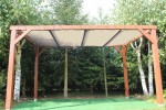 Brązowa drewniana pergola z zamontowanym beżowym przeciwsłonecznym dachem żaglowym HDPE na wymiar w ogrodzie.