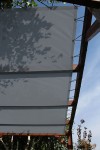 Szary, prostokątny dach żaglowy przeciwsłoneczny z HDPE zamontowany na drewnianej pergoli za pomocą linek.