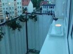 Biała osłona balkonowa na wymiar zamontowana na balustradzie, obok doniczki z kwiatami i kieliszek wina.