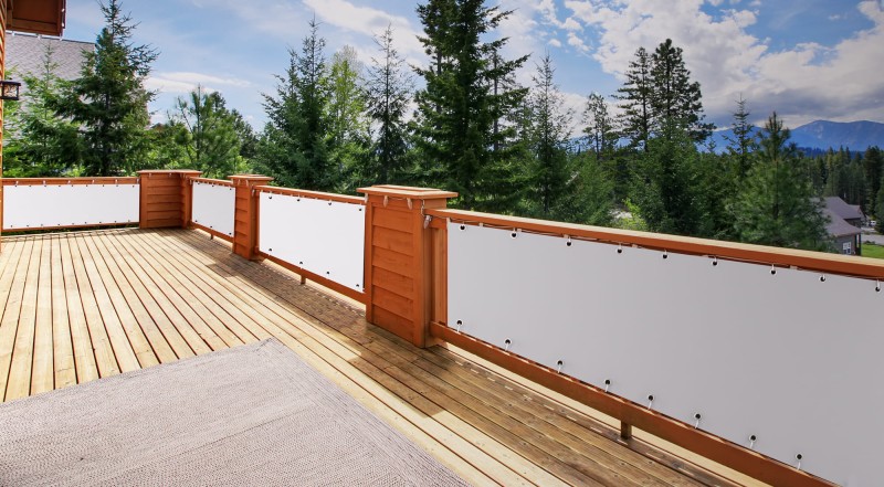 Biała osłona balkonowa na wymiar zamontowana na drewnianej barierce dużego tarasu z widokiem na las i góry.